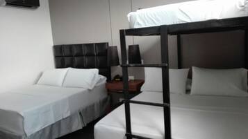 A hotel room with two beds, one with a black headboard and the other with a white headboard. There is a small table with a lamp and a red object on it.