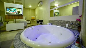 A modern bathroom with a large bathtub, a television mounted on the wall, and a mirror above the sink.