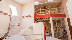 A modern bathroom with a bathtub, a shower, and a mirror. There is a staircase leading to an upper level with a balcony.