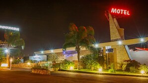 A motel with a prominent 'Motel' sign, a large billboard advertising 'Pousada', and a well-lit entrance area.