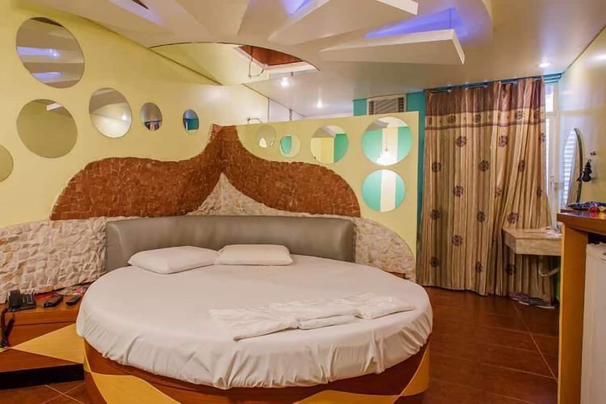 A circular bed with a stone-like headboard, a wall with circular mirrors, and a bathroom with a shower curtain.