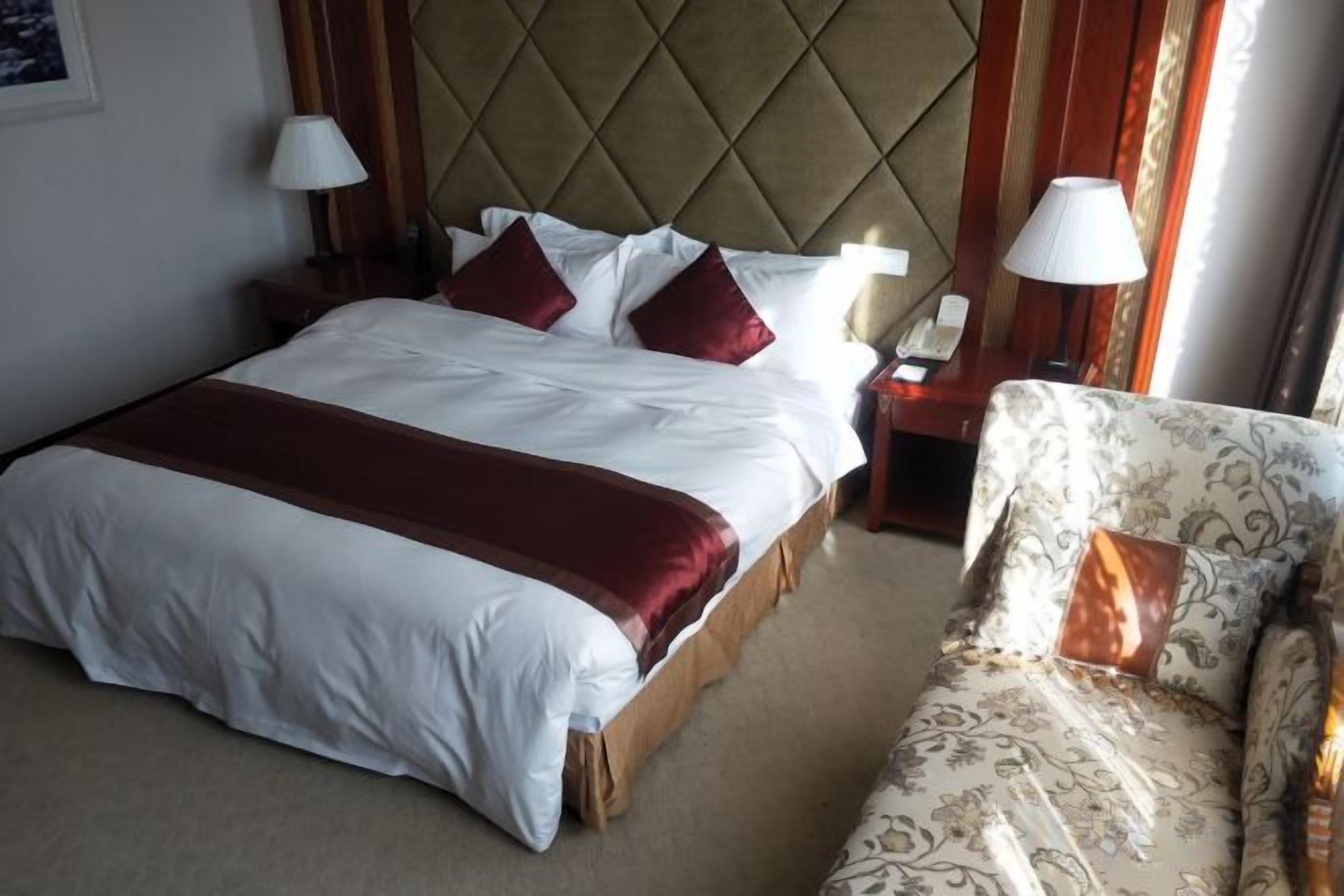 A hotel room with a large bed, bedside tables, a chair, and a lamp.