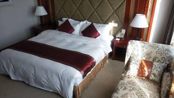 A hotel room with a large bed, bedside tables, a chair, and a lamp.