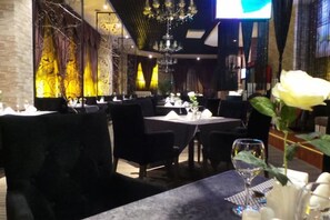 L’intérieur d’un restaurant, avec des tables dressées pour le service, des chaises et un lustre.