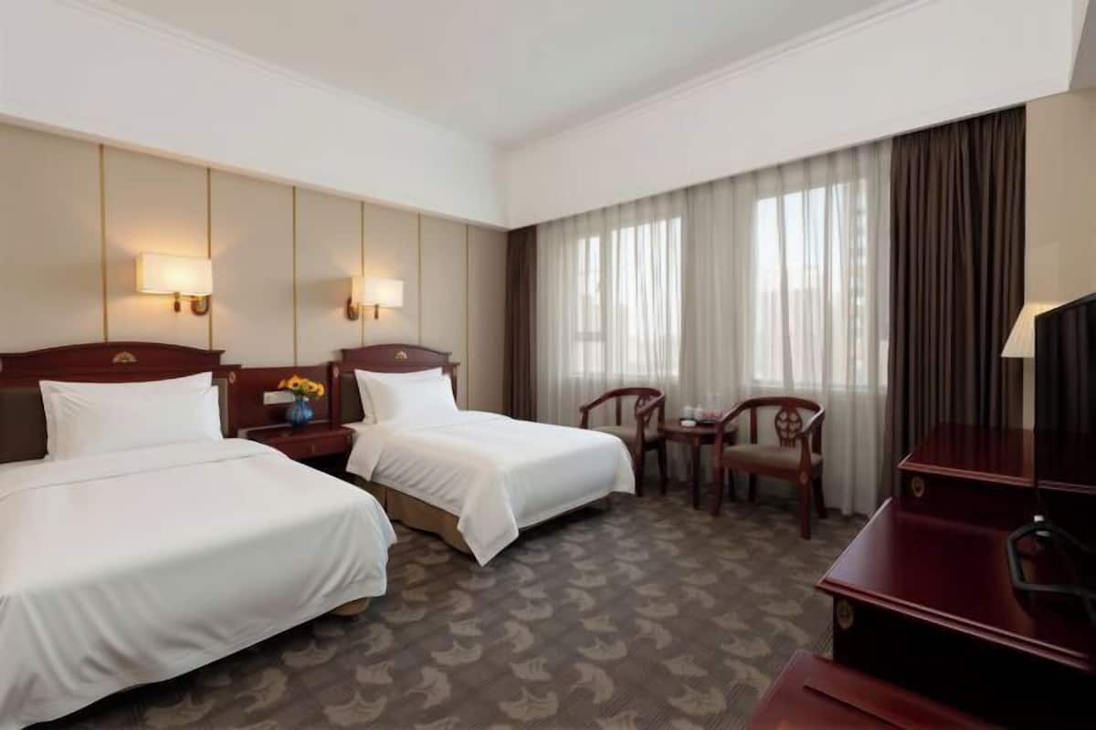 Habitación de hotel con dos camas, un escritorio, una silla, un televisor y una ventana con cortinas.