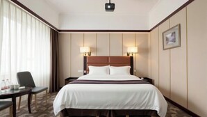 A hotel room with a large bed, two bedside lamps, a desk with a chair, and a window with curtains. - Grand View International Hotel (LIAOYANG)
