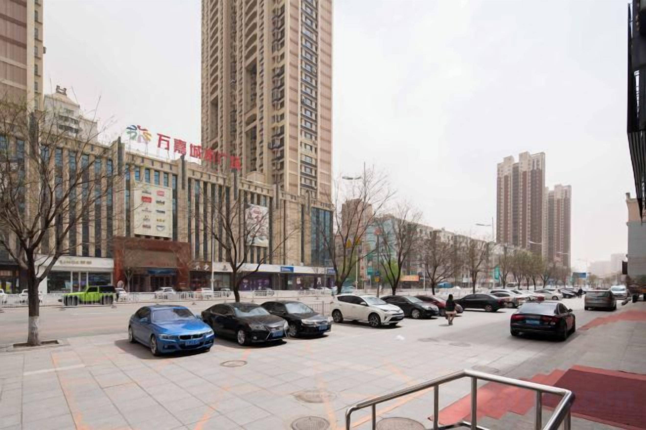 A parking lot with multiple cars, a pedestrian walkway, and tall buildings in the background.