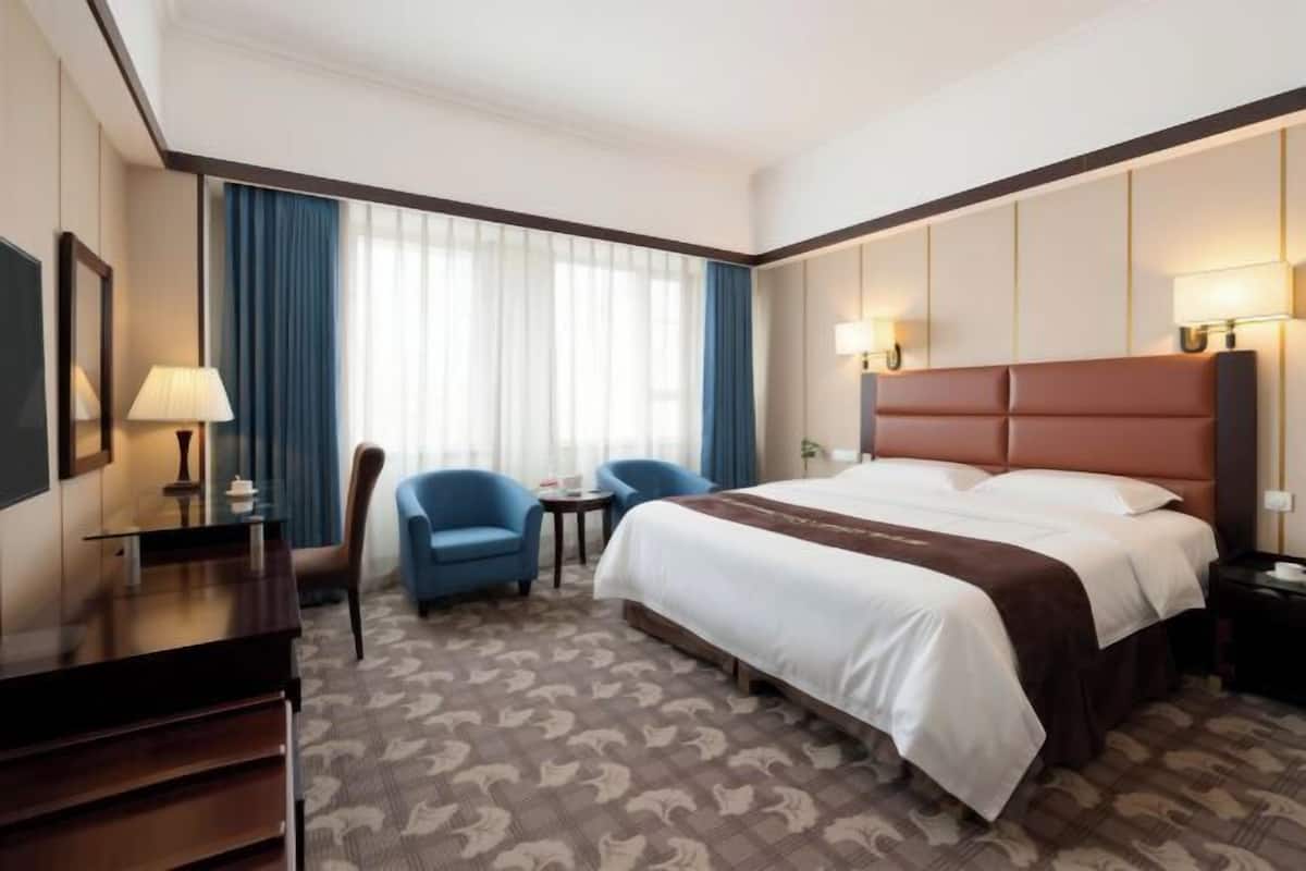 Una habitación de hotel con una cama grande, dos sillones, un escritorio y una lámpara.