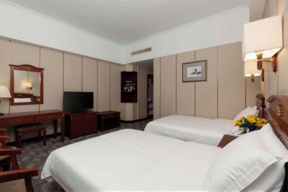 A hotel room with two beds, a desk, a TV, and a mirror.