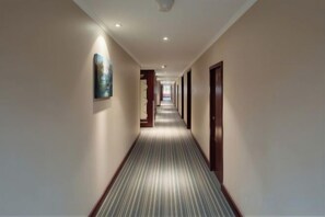 A hotel corridor with a carpeted floor, doors on both sides, and a painting on the left wall. - Grand View International Hotel (LIAOYANG)