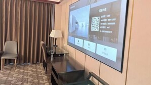 A hotel room with a large screen displaying room information, a desk with a lamp, a chair, and a patterned rug. - Grand View International Hotel (LIAOYANG)