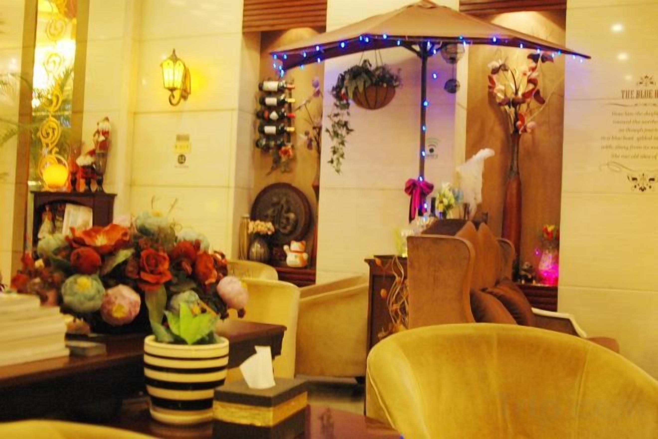 A hotel lobby with a reception desk, a seating area with chairs, and a decorative plant arrangement.