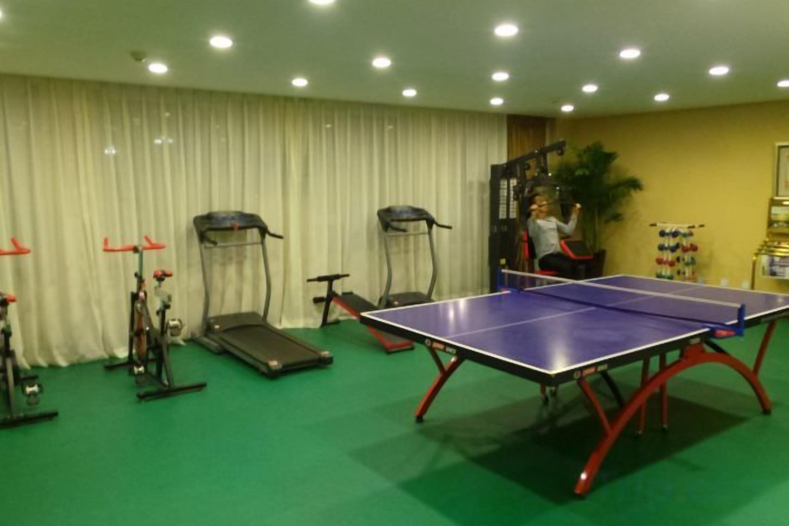 A room with a ping pong table, exercise equipment, and a curtain.