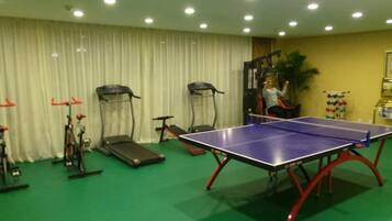 A room with a ping pong table, exercise equipment, and a curtain.