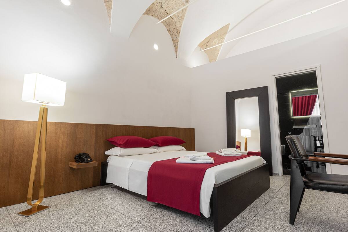A hotel room with a bed, bedside table, lamp, and a mirror.