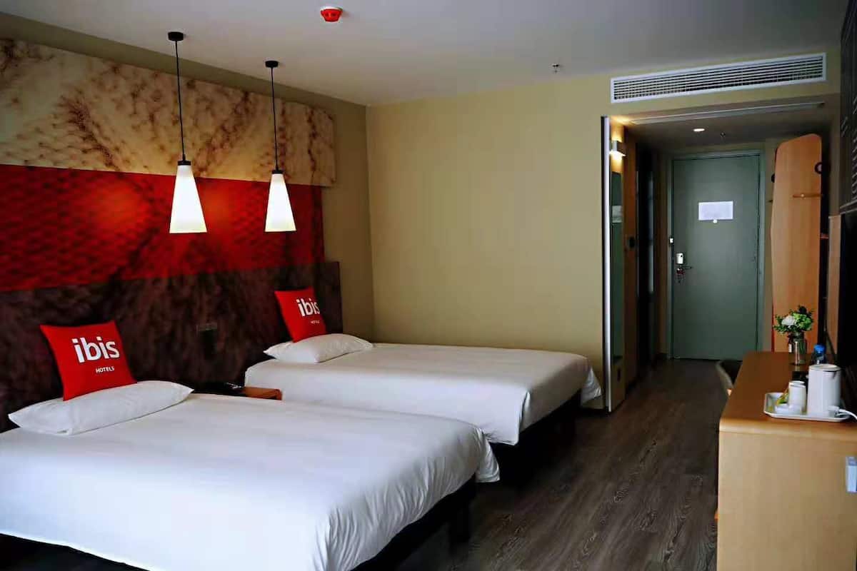 Habitació d'hotel amb dos llits, barra minibar i disseny de paret vermell i beix.