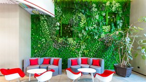 Un área de descanso moderna con sofás grises y cojines rojos, sillones mecedores blancos y una pared vertical con jardín.