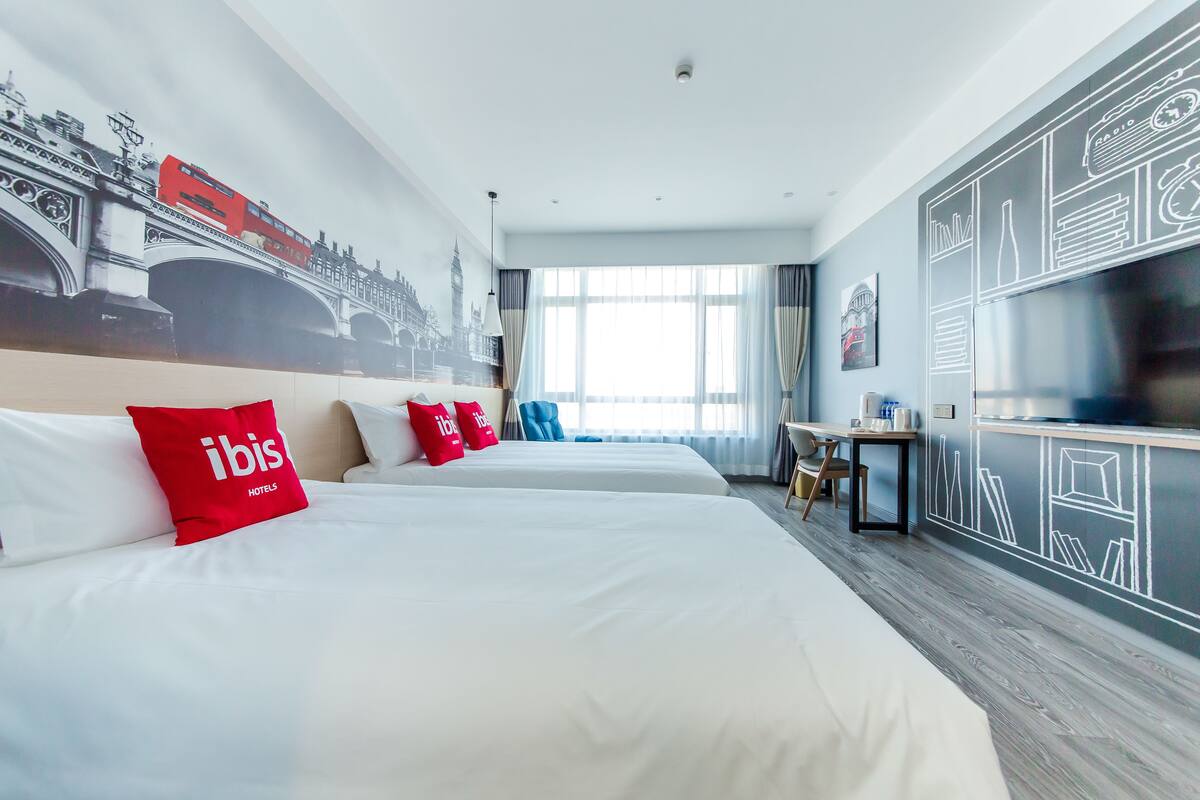 Een hotelkamer met twee bedden, een bureau, een stoel en een groot raam.