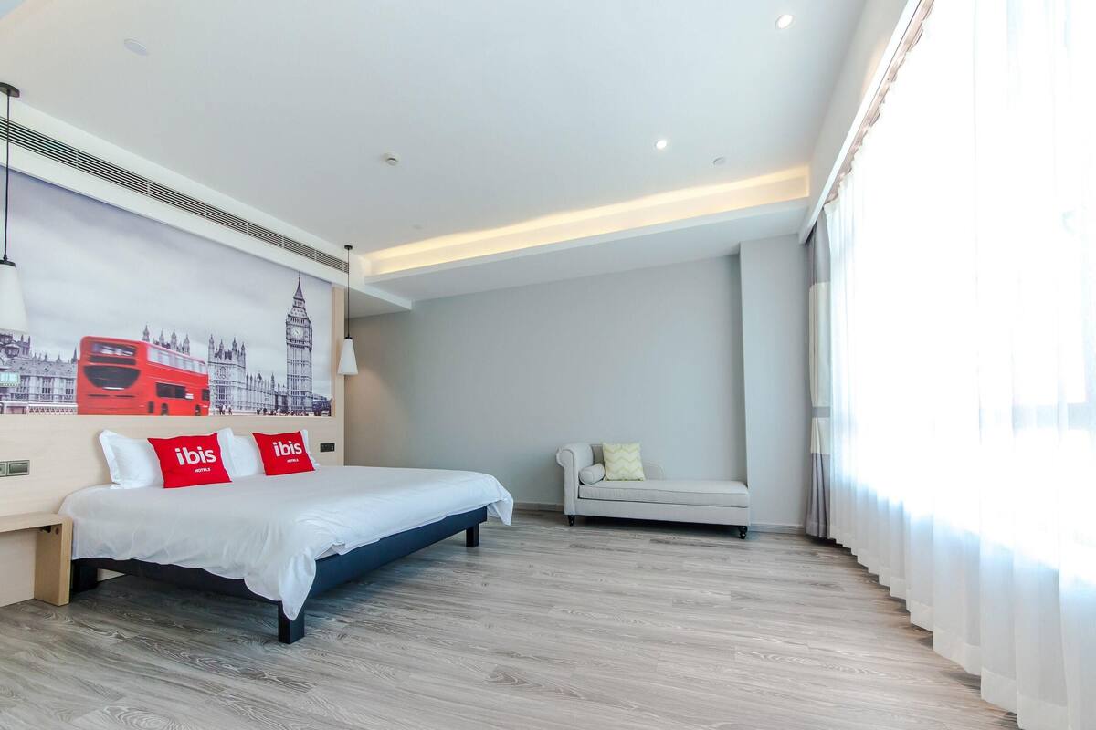 Een moderne hotelkamer met een groot bed, een slaapbank en een kunstwerk aan de muur van een rode dubbeldekkerbus.