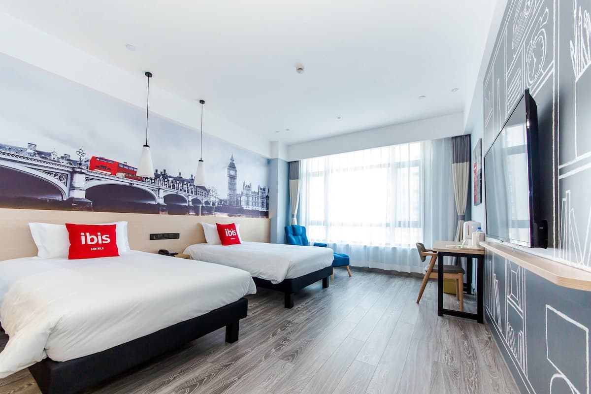 Een hotelkamer met twee bedden, een bureau, een televisie en een groot raam met gordijnen.