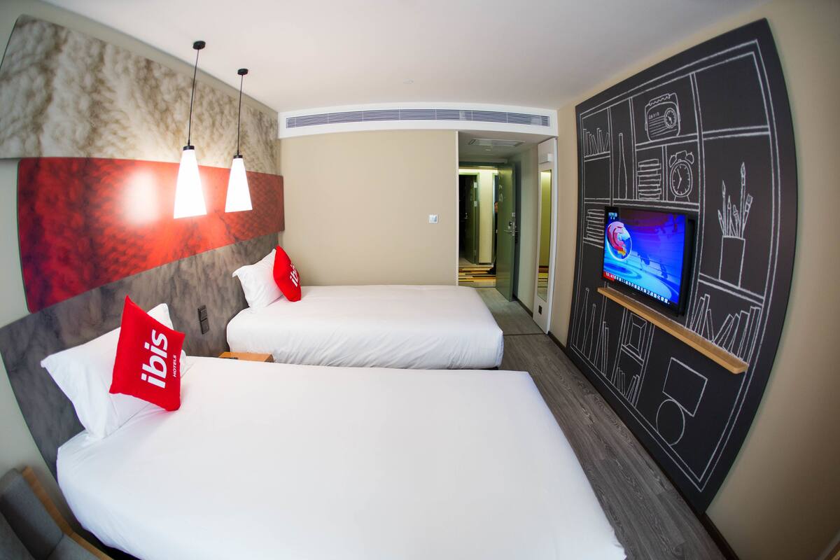Ein Hotelzimmer mit zwei Betten, einem Fernseher und einer Wand mit einer Uhr und weiteren Symbolen.