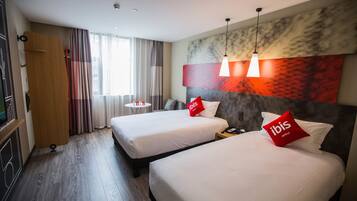 Habitación de hotel con dos camas, un escritorio, una silla y un ventanal con cortinas.