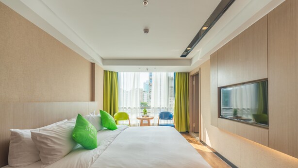 Quarto de hotel com uma cama grande, televisão e vista para a cidade pela janela.