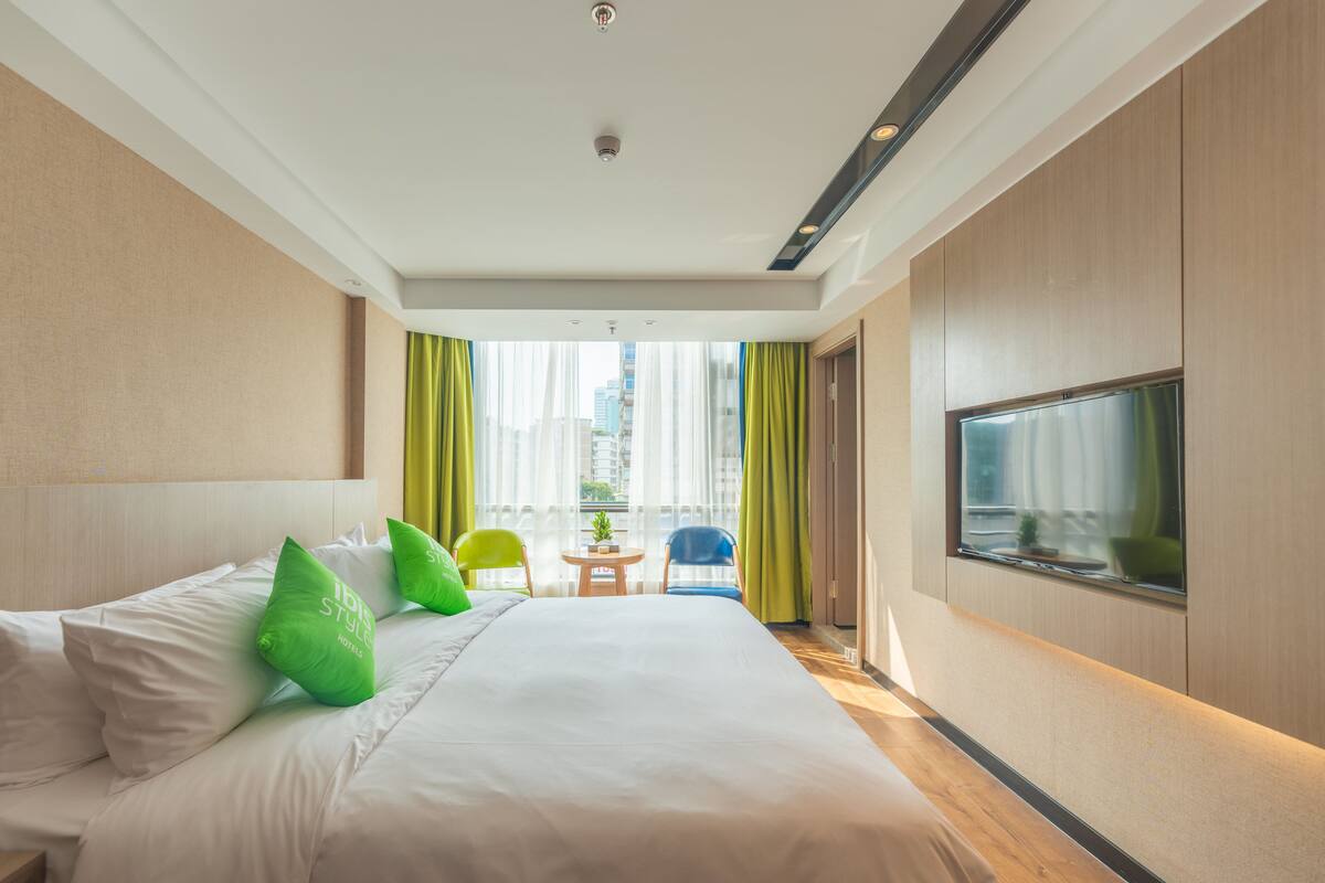 Habitación de hotel con una cama grande, televisión y vistas a la ciudad por la ventana.
