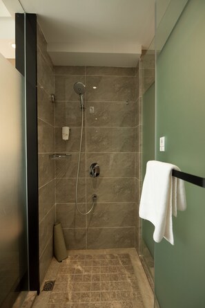 Una ducha moderna con cabezal de ducha de mano, dispensador de jabón en la pared y un perchero para toallas.