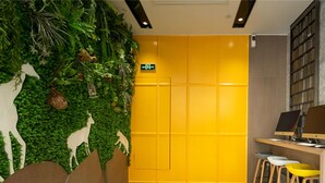 Quarto com porta amarela, parede verde decorada com recortes de animais e uma escrivaninha com duas cadeiras.