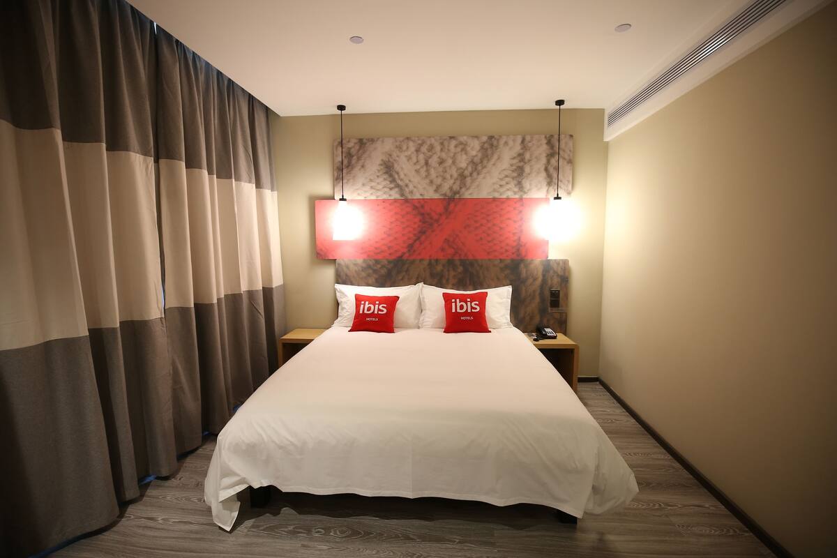 A hotel room with a large bed, two bedside tables, a nightstand, and a wall-mounted lamp.