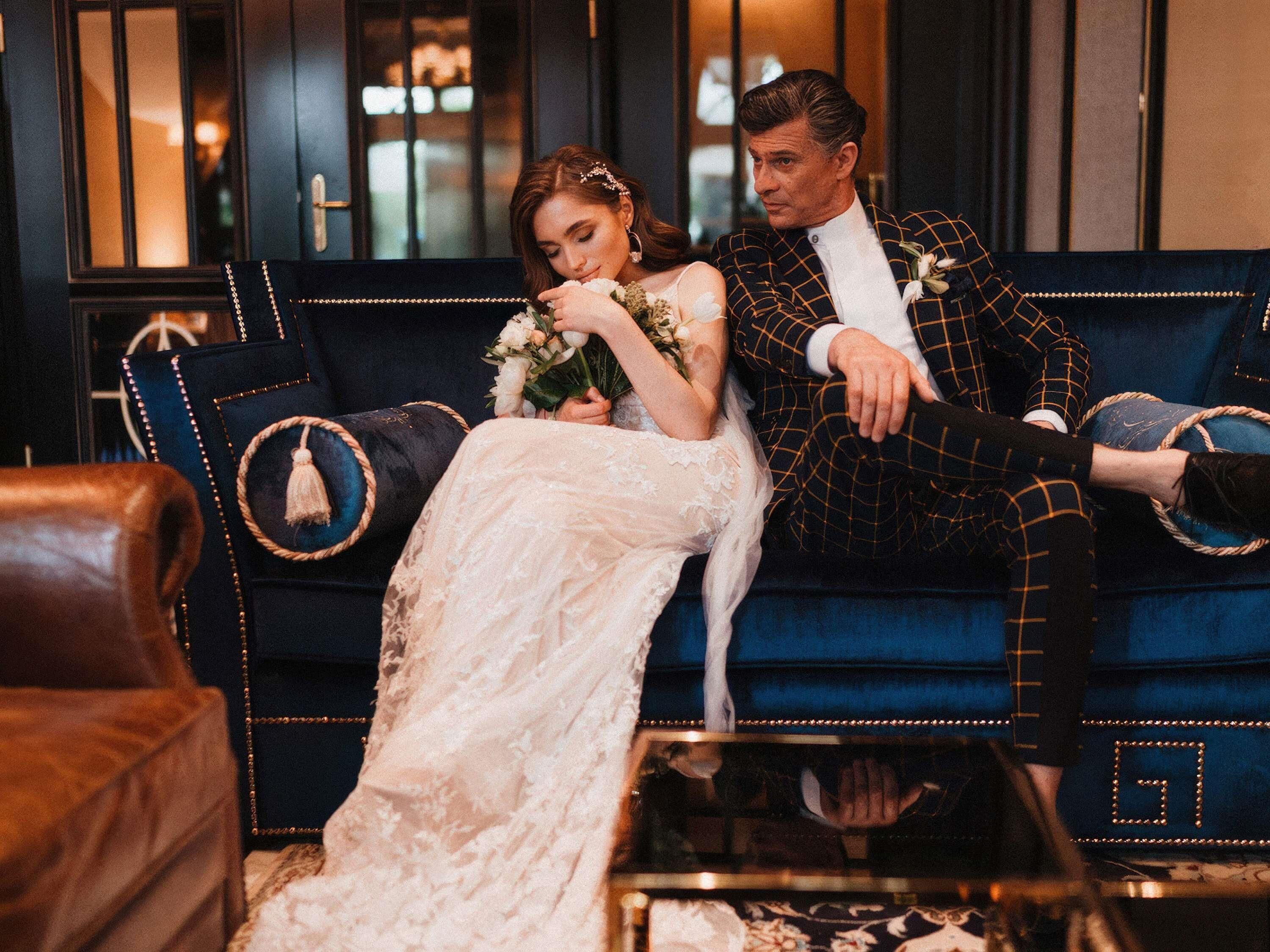 A couple seated on a dark blue sofa with gold trim, in a room with dark wood paneling and a glass partition.
