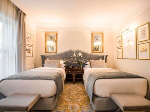 Una habitación de hotel con dos camas, un espejo grande y decorativo, y cuadros en las paredes.