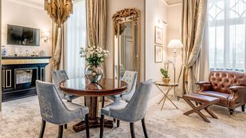 A formal dining room with a round table, chairs, a chandelier, a fireplace, a large mirror, and a leather armchair.