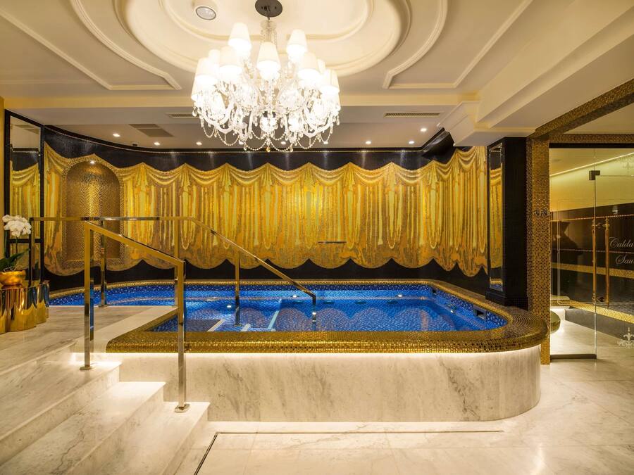 A luxurious indoor pool area with a marble floor, a golden curtain backdrop, and a chandelier.