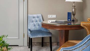 A hotel room with a round wooden table, a blue upholstered chair, a lamp, and a television mounted on the wall.