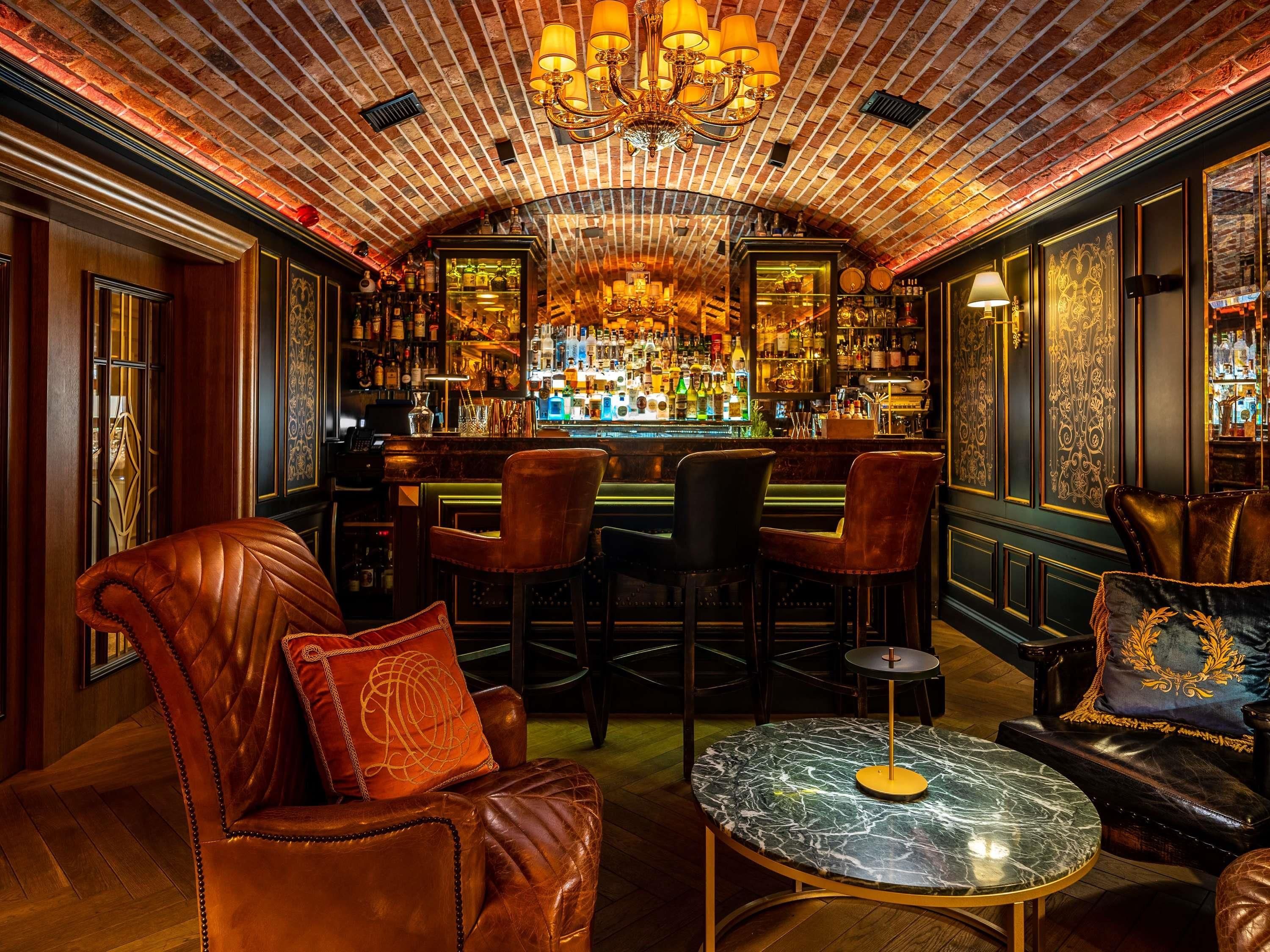 A bar area with leather chairs, a marble table, and a brick ceiling.