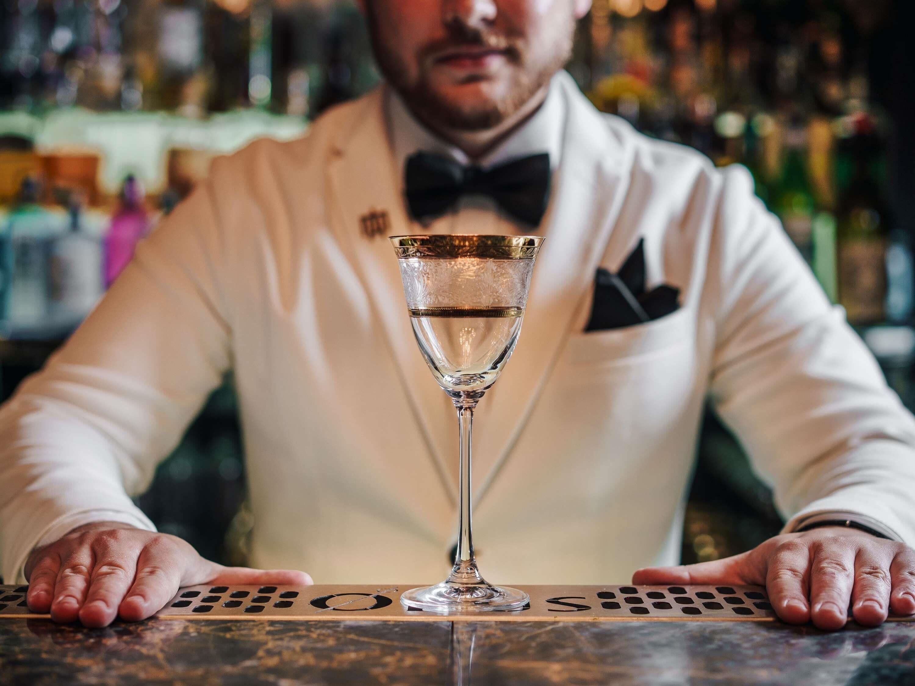 Ein Barkeeper im weißen Anzug mit Fliege, der ein Cocktailglas hält.