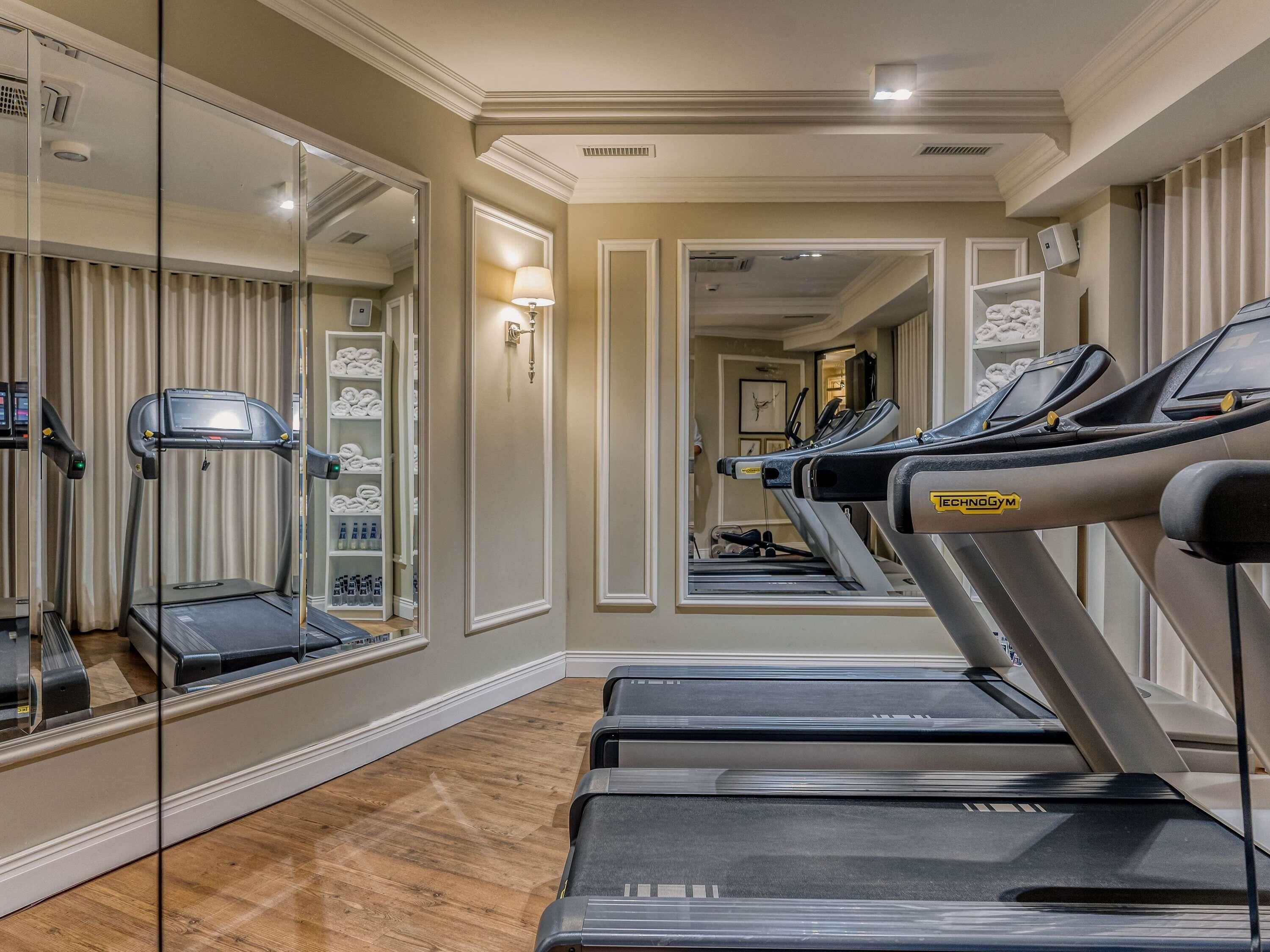 A hotel gym with treadmills, a mirrored wall, and a storage unit with towels.