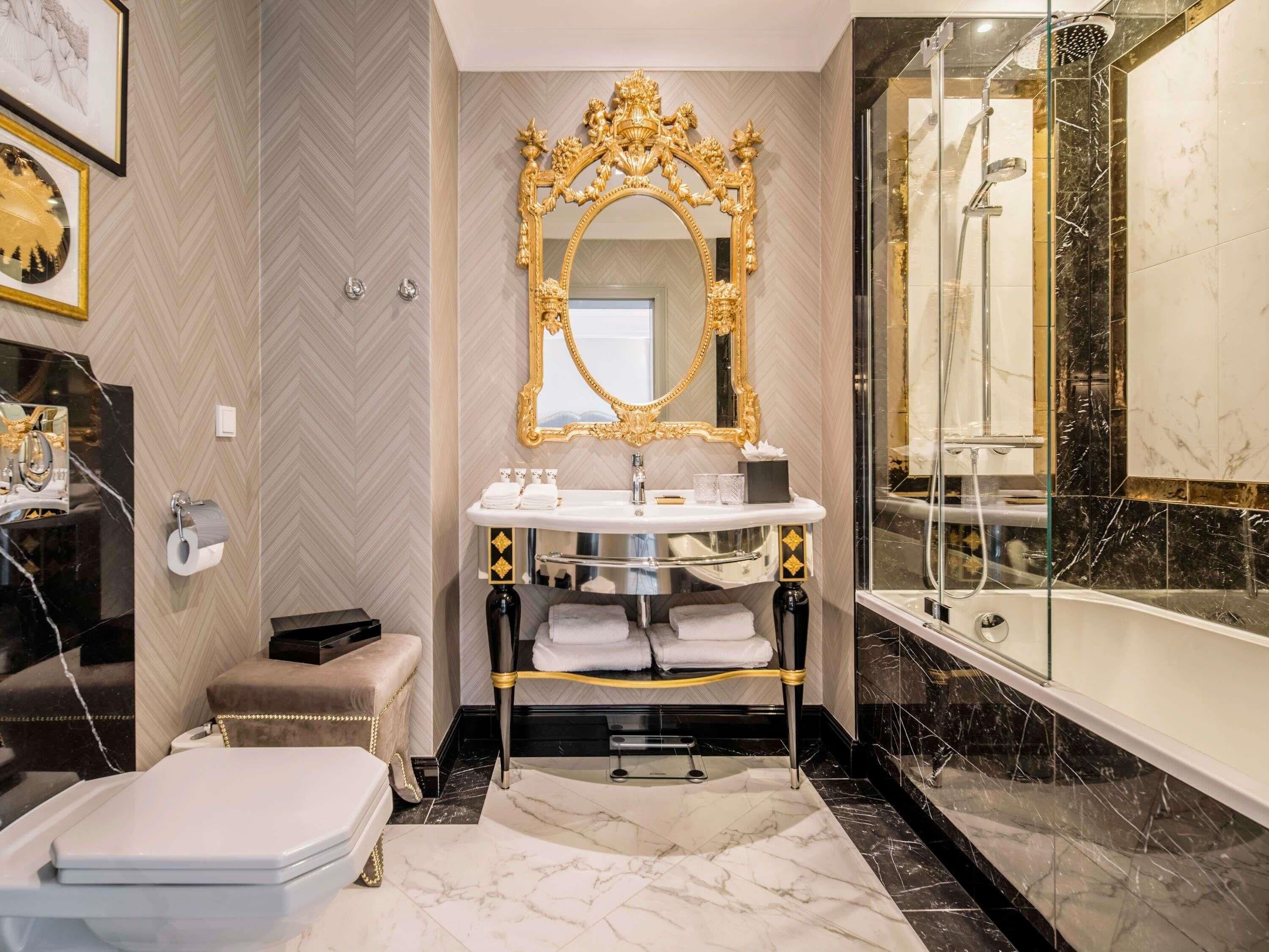 A luxurious bathroom with a marble floor, a gold-framed mirror, a bathtub, and a shower.