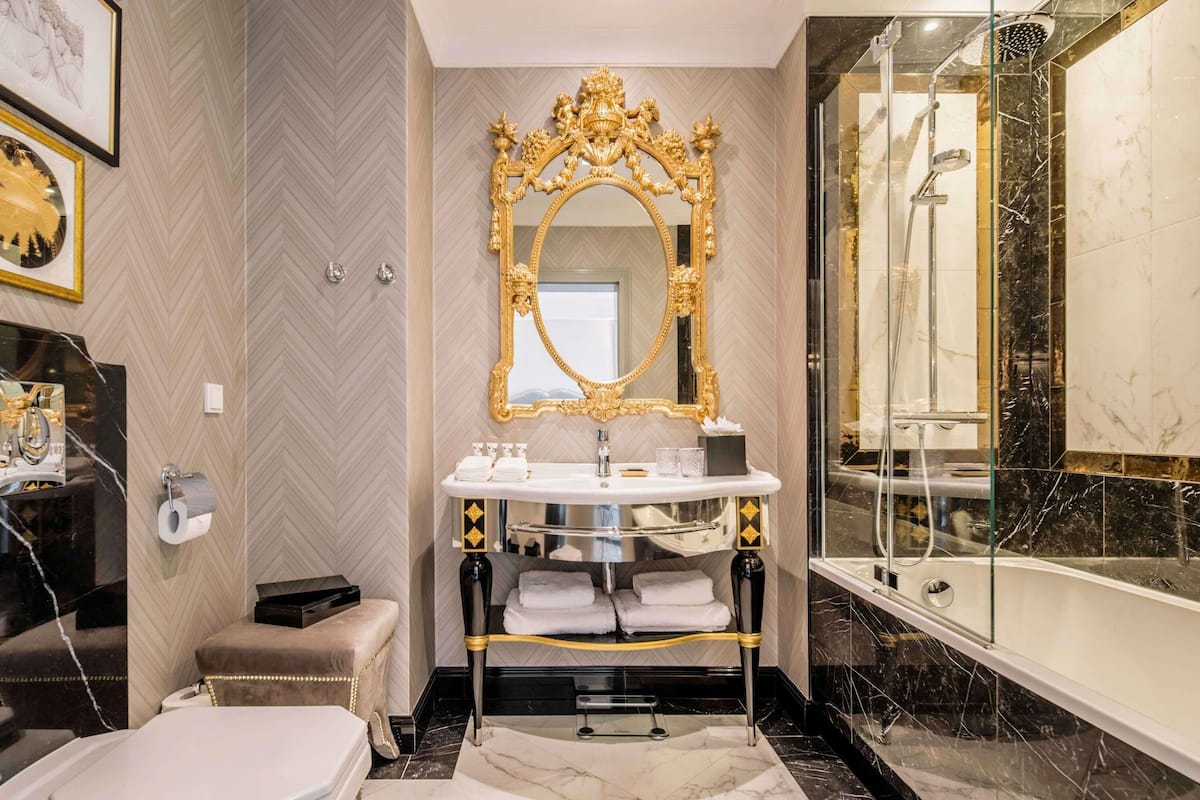 A luxurious bathroom with a marble floor, a gold-framed mirror, a bathtub, and a shower.