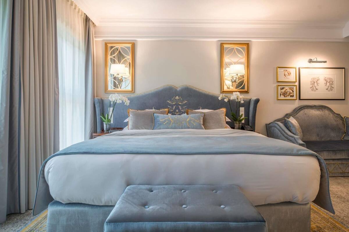 Una cama grande con cabecera capitonada, una mesita de noche con lámpara y un banco.