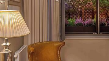 Una habitación con vista a un jardín a través de una ventana, una mesa con una taza y una lámpara.
