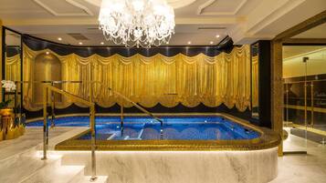 A luxurious indoor pool area with a marble floor, a grand chandelier, and a gold curtain backdrop.