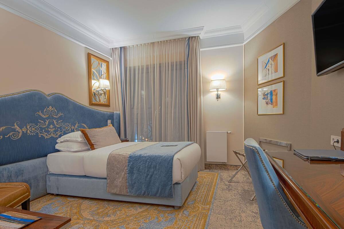 Una habitación de hotel con una cama grande, un escritorio, una silla, una lámpara y un televisor.