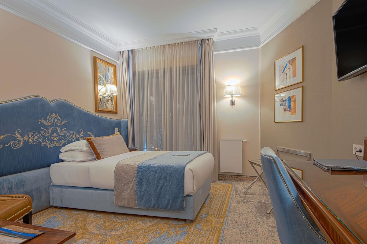 A hotel room with a large bed, a desk, a chair, a lamp, and a television.