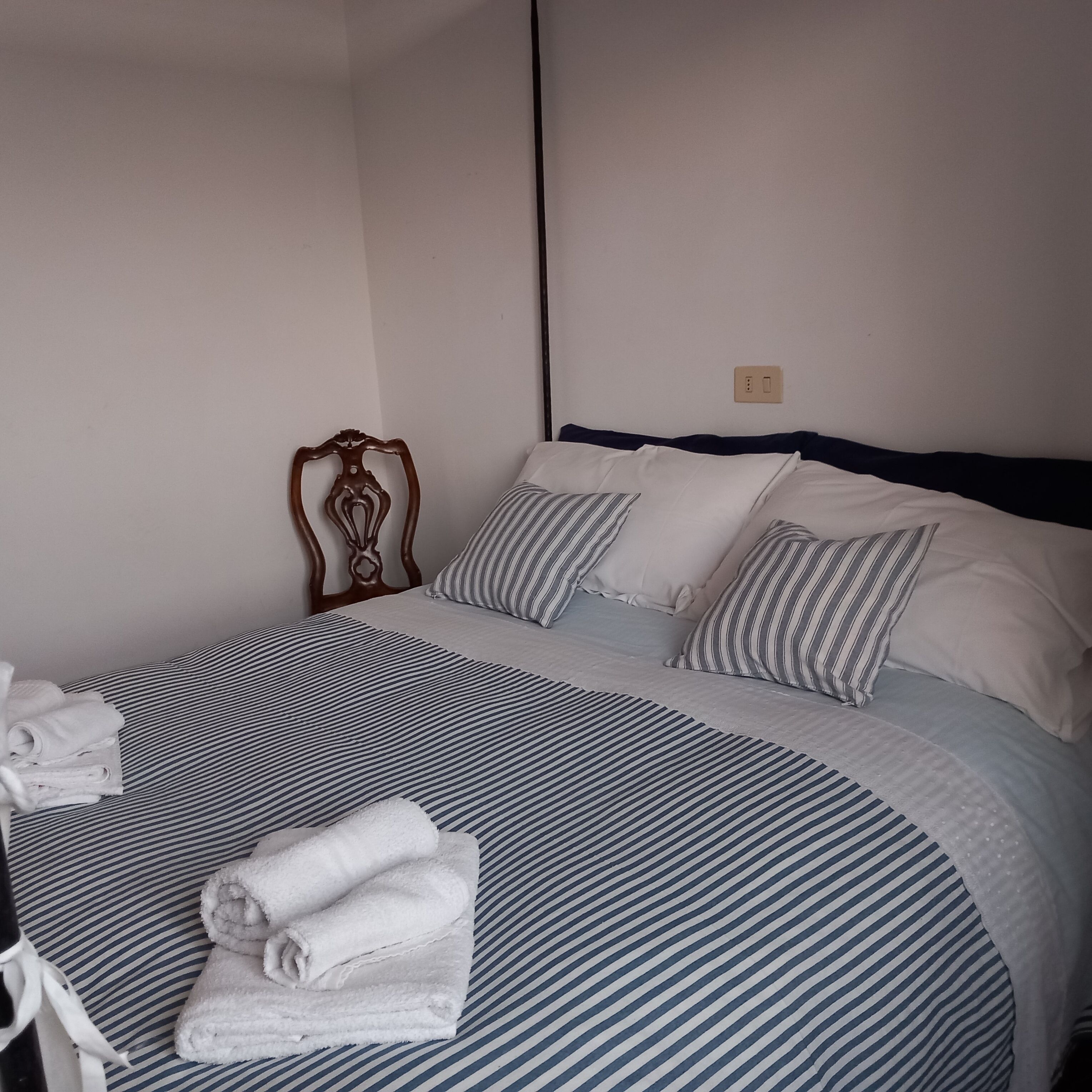 A neatly made bed with striped bedding and pillows, a wooden headboard, and folded towels on the side.