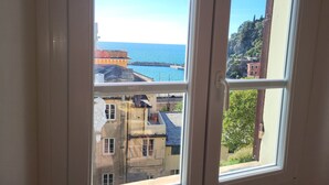 Une fenêtre donnant sur une ville côtière, des bâtiments et un ciel dégagé.