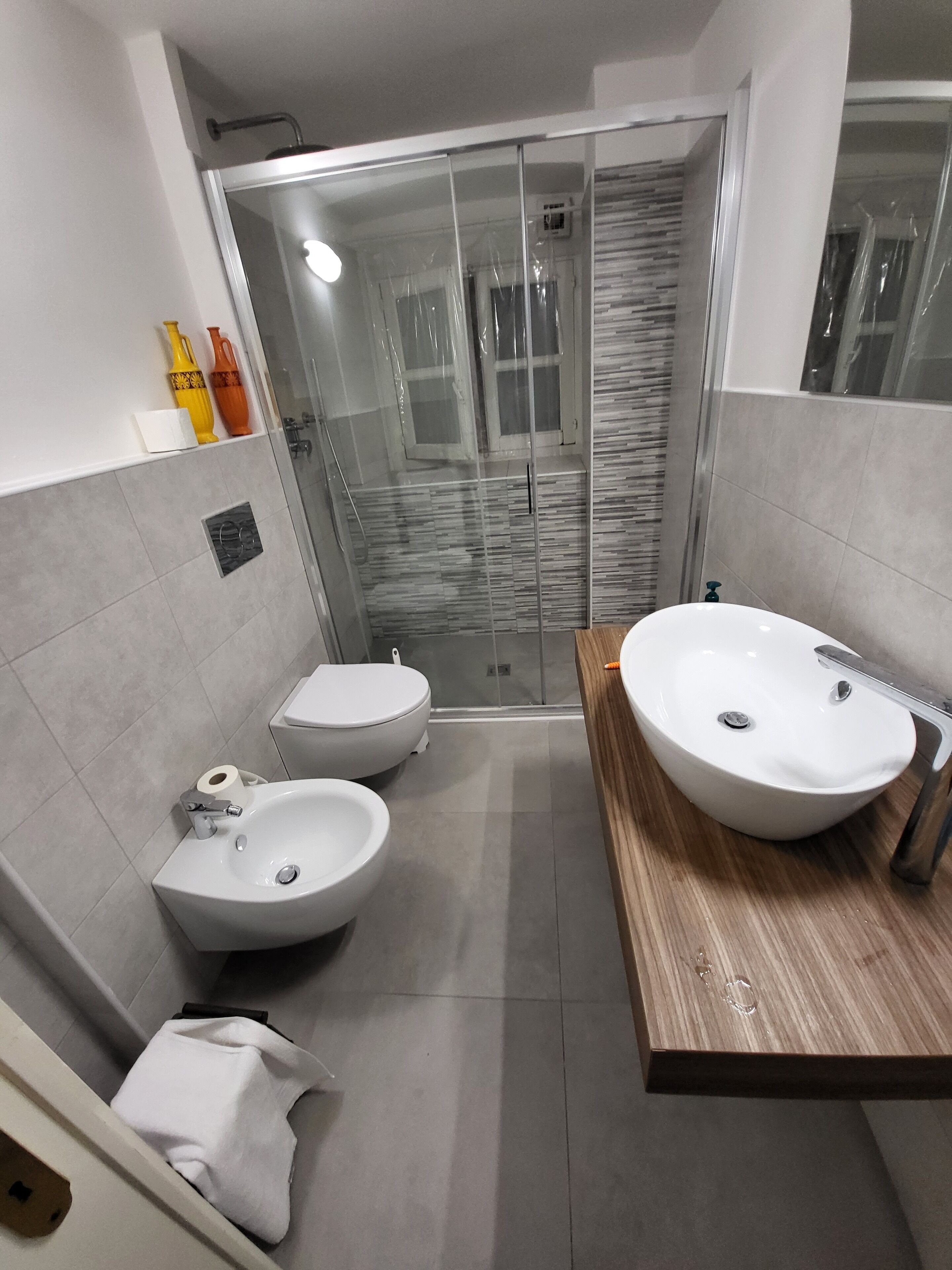 A modern bathroom with a glass-enclosed shower, two toilets, a large sink, and a wooden vanity.