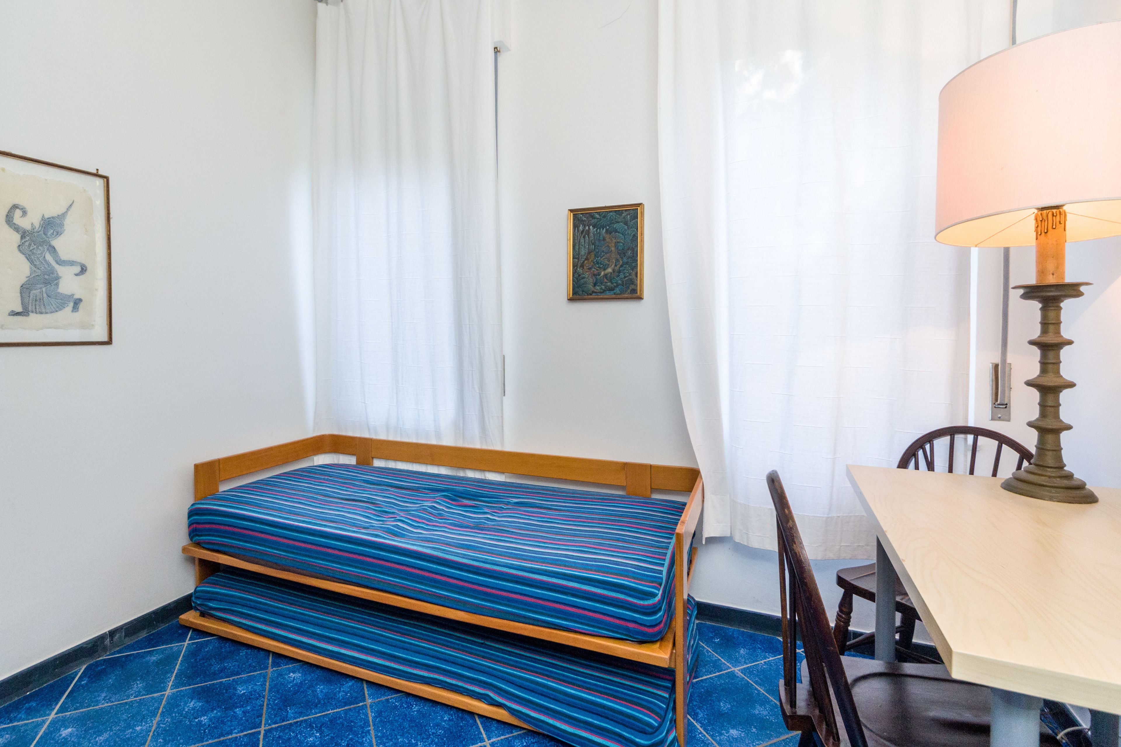 A small room with a bed, a table with a lamp, and a chair.